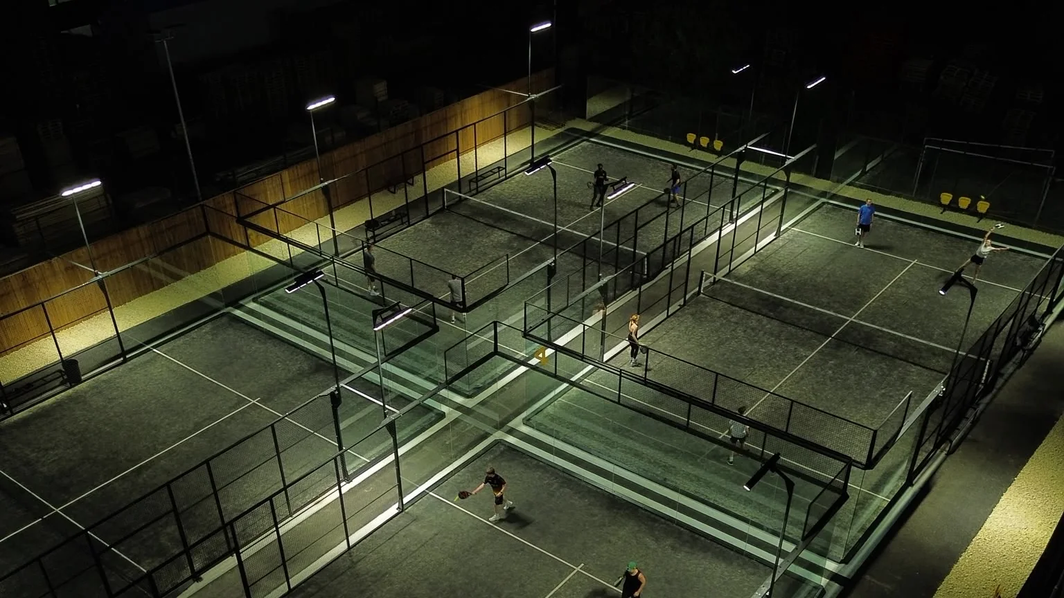 Four floodlit padel courts at Pukka Padel Leeds at night, seen from above, with players mid-rally.