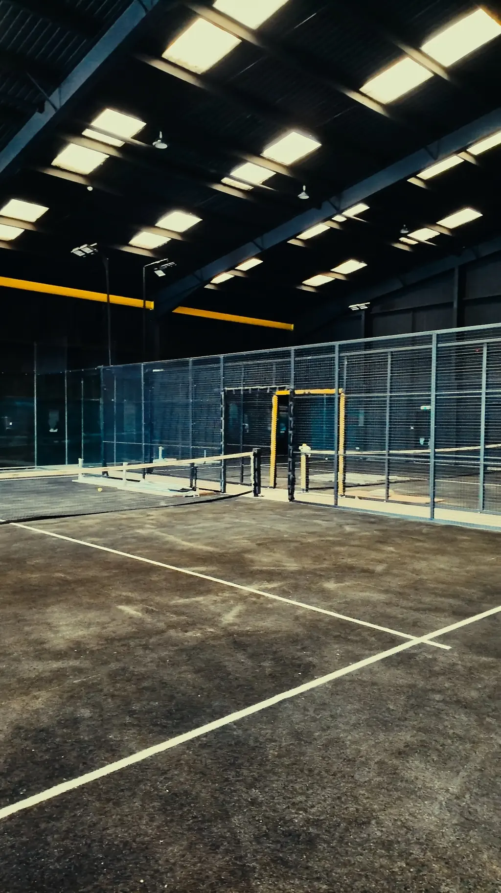 The glass back wall of an indoor court at Pukka Padel Kidderminster, lit.
