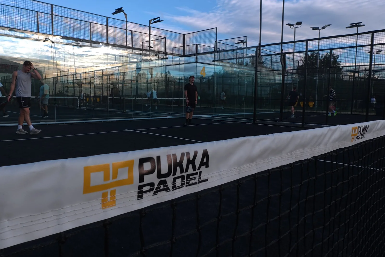 Players on the outdoor courts at Pukka Padel Leeds behind a branded windbreak.