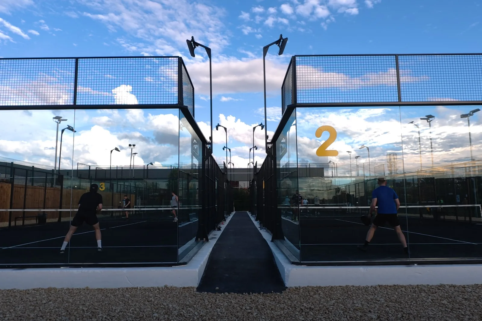 Two players walking towards court 2 at Pukka Padel Leeds under a blue sky.